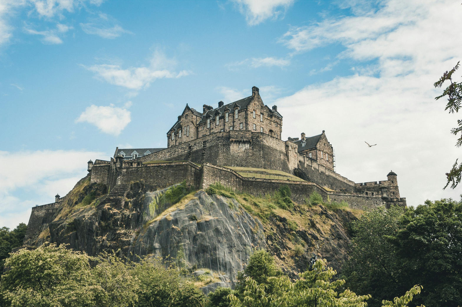 Edinburgh Castle on its rock, above trees, under a bright sky.
