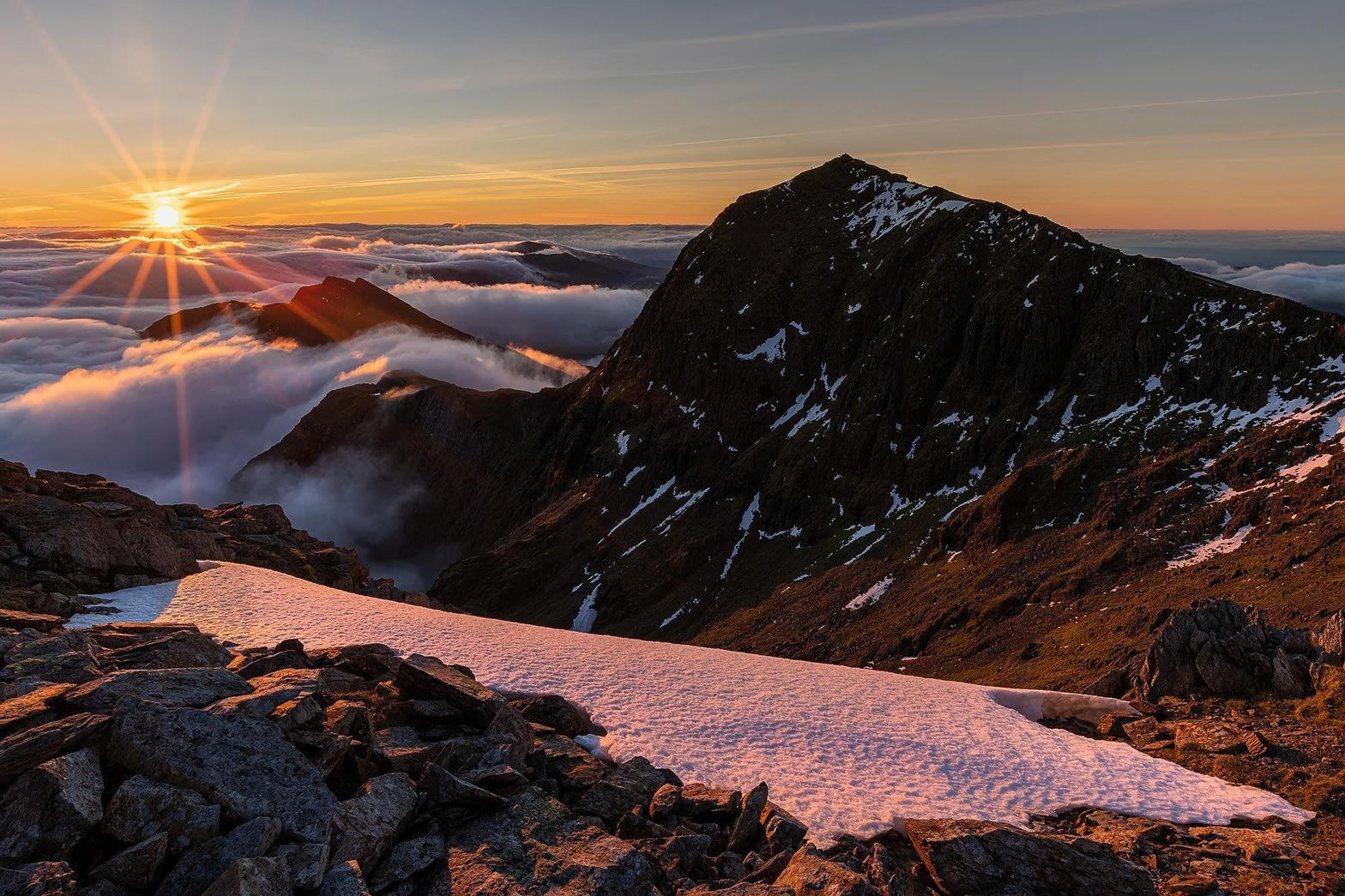 Sunrise over a snow-dusted ridge in Eryri, with cloud filling the valleys below.