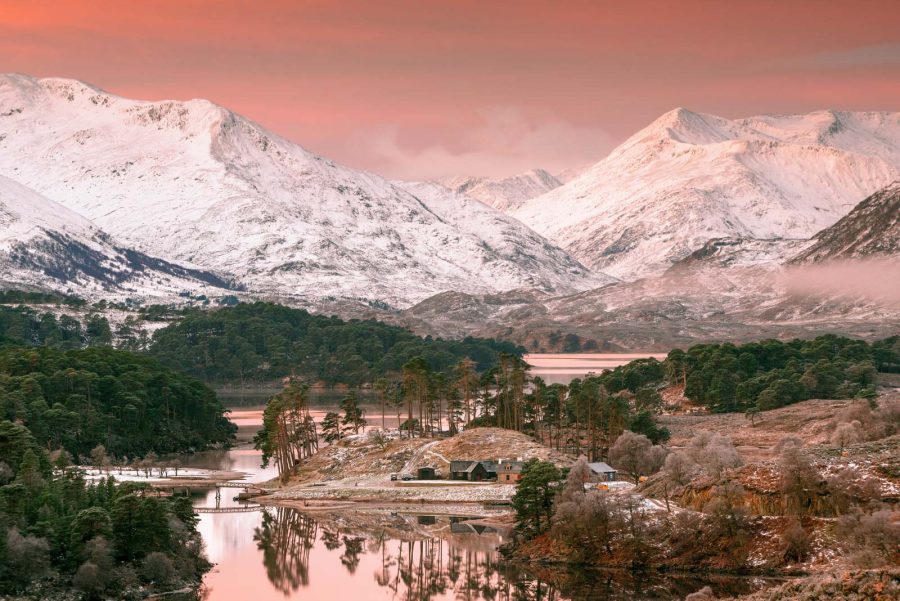 Snow-covered Highland mountains reflected in a loch at a pink dusk.