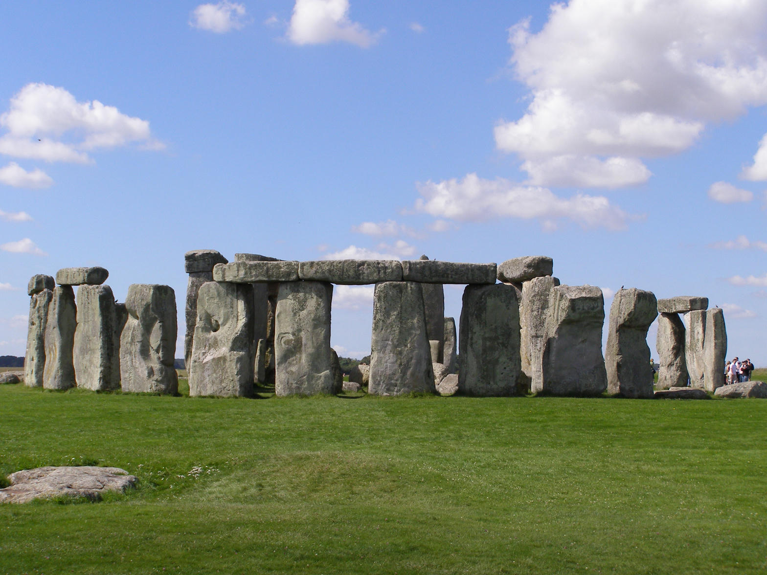 The standing stones of Stonehenge on open grassland under a blue sky.
